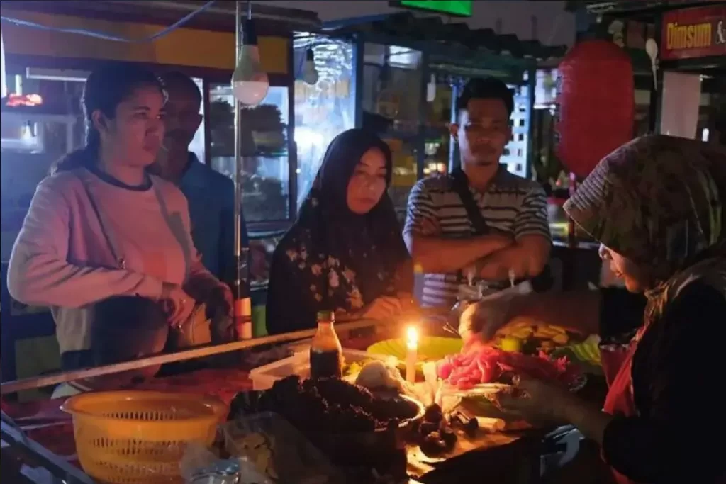 Pedagang melayani pembeli menggunakan penerangan lilin saat terjadi gangguan pasokan listrik di Denpasar, Bali, Jumat (2/5/2025). ANTARA FOTO/Nyoman Hendra Wibowo/Spt.